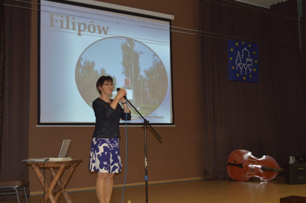 Na zdjęciu nauczycielka historii, Pani Katarzyna Panek przemawiająca do mikrofonu ze sceny.