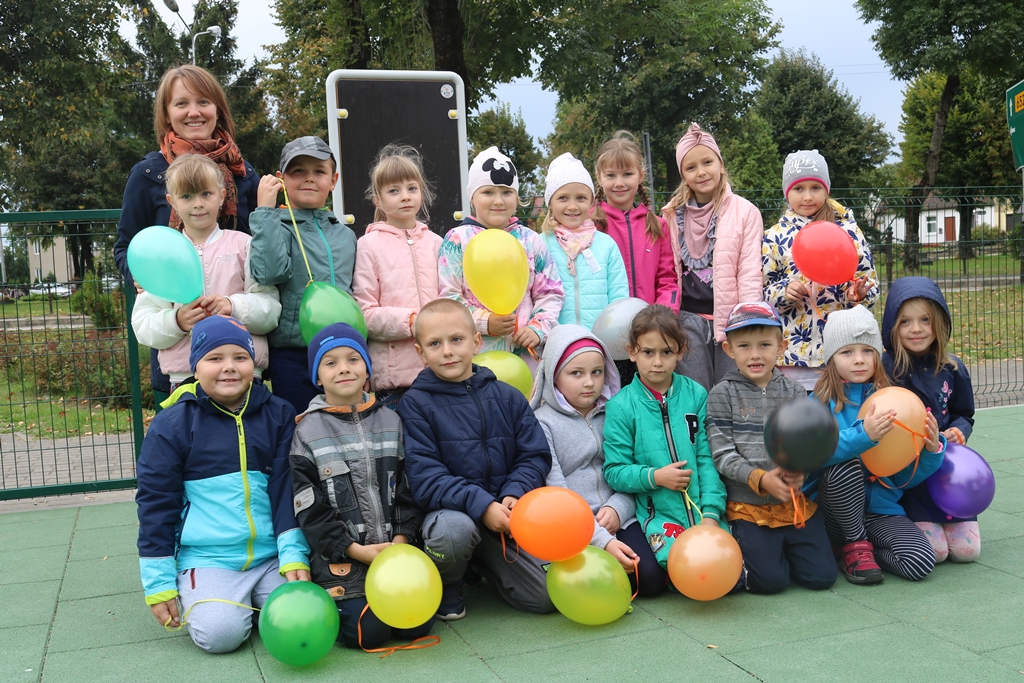 Zdjęcie przedstawia szesnaścioro dzieci z balonikami stojących w dwóch rzędach oraz ich wychowawczynię.