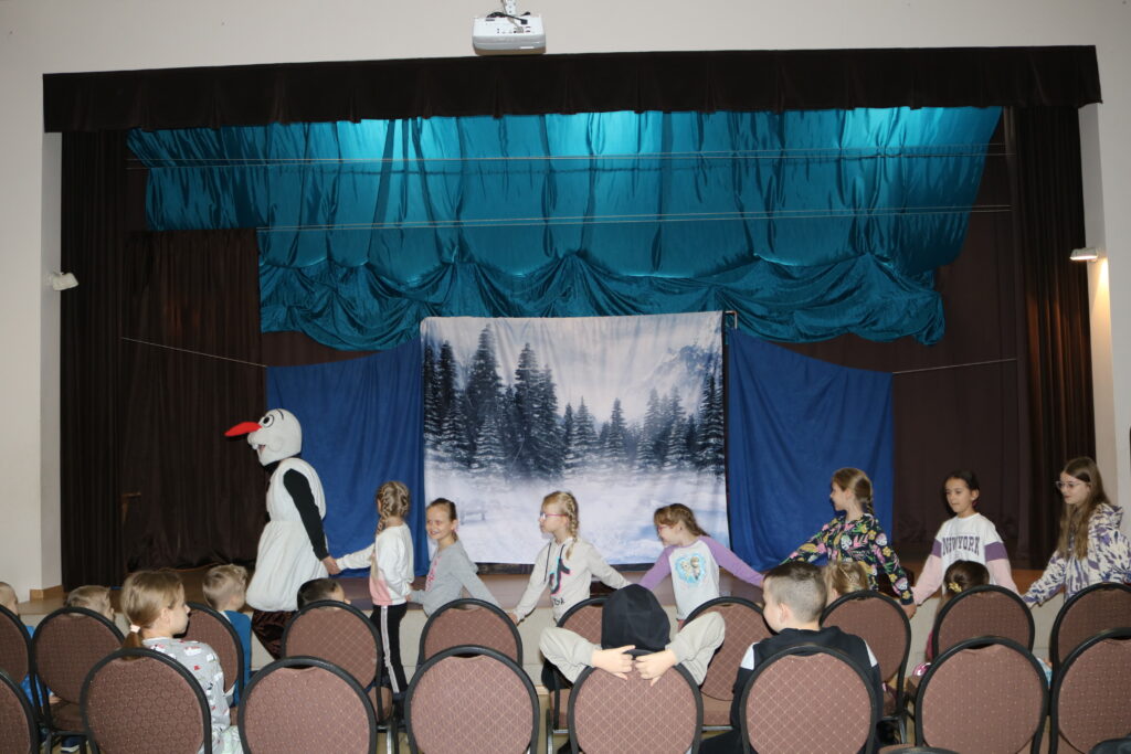 Bałwan Olaf, pod sceną bawi się z dziećmi ,przybyłymi na przedstawienie. Dzieciaki trzymając się za ręce, podążają za Olafem po całej sali.